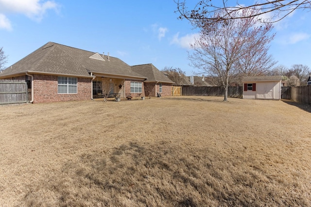 rear view of house with brick siding, a shingled roof, a fenced backyard, an outbuilding, and a storage unit