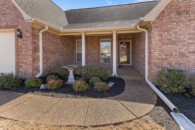 view of exterior entry with brick siding, covered porch, a shingled roof, and a garage