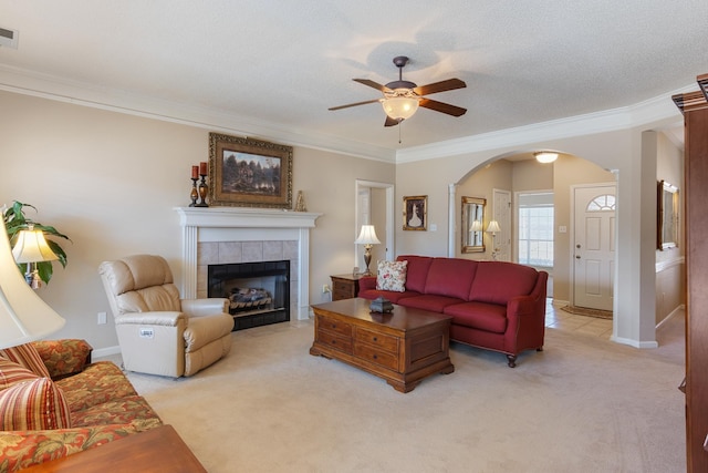 living area featuring visible vents, a tiled fireplace, light colored carpet, arched walkways, and a ceiling fan