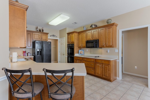 kitchen featuring black appliances, a peninsula, brown cabinetry, light countertops, and light tile patterned floors