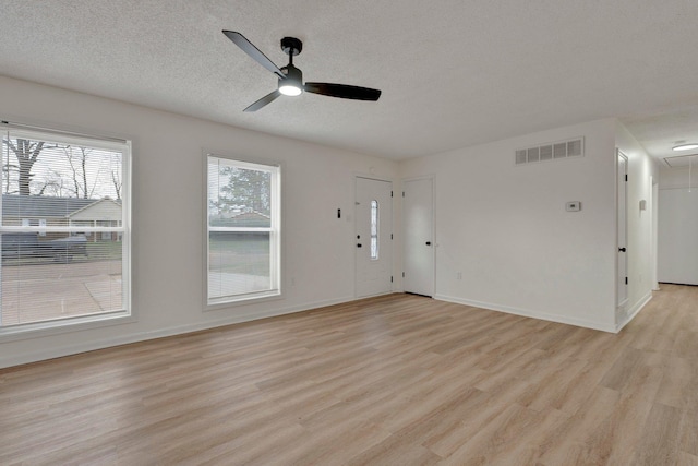 unfurnished living room featuring attic access, light wood-style flooring, a ceiling fan, and visible vents