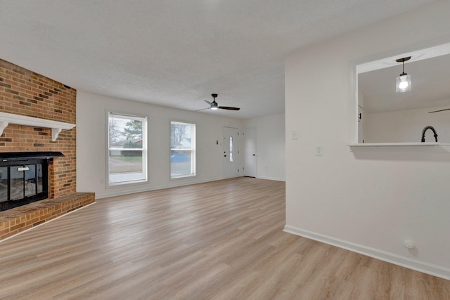 unfurnished living room with a ceiling fan, baseboards, light wood-style flooring, a textured ceiling, and a brick fireplace