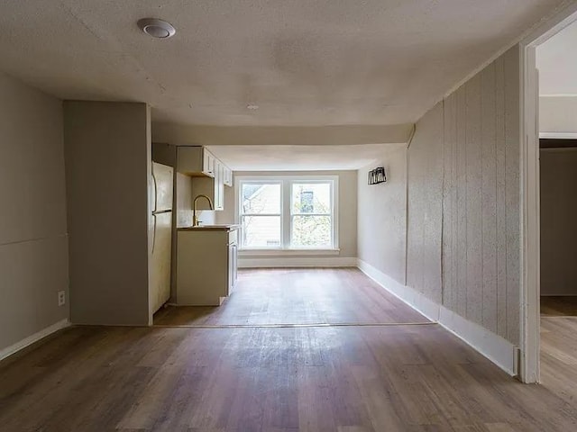 unfurnished room featuring wooden walls, light wood-type flooring, baseboards, and a sink