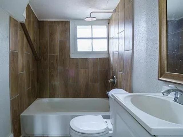 full bathroom featuring vanity, toilet, shower / bathtub combination, and a textured wall