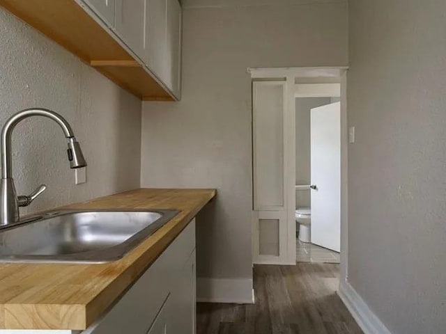 kitchen with dark wood-type flooring, white cabinets, baseboards, and a sink