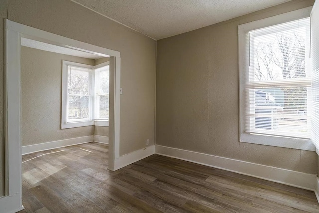 spare room featuring baseboards, a textured ceiling, dark wood-style flooring, and a textured wall