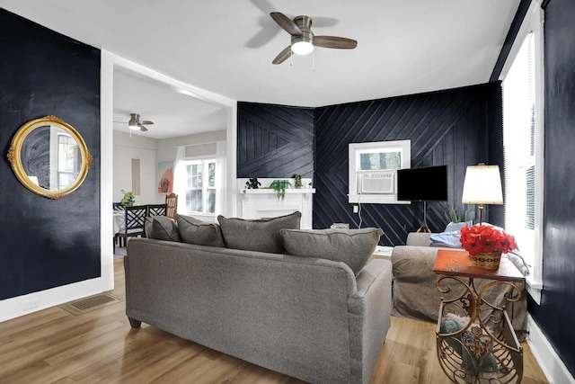 living area with an accent wall, wood finished floors, and ceiling fan