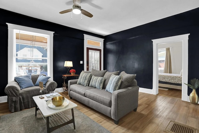 living area featuring baseboards, visible vents, a ceiling fan, and light wood-style floors