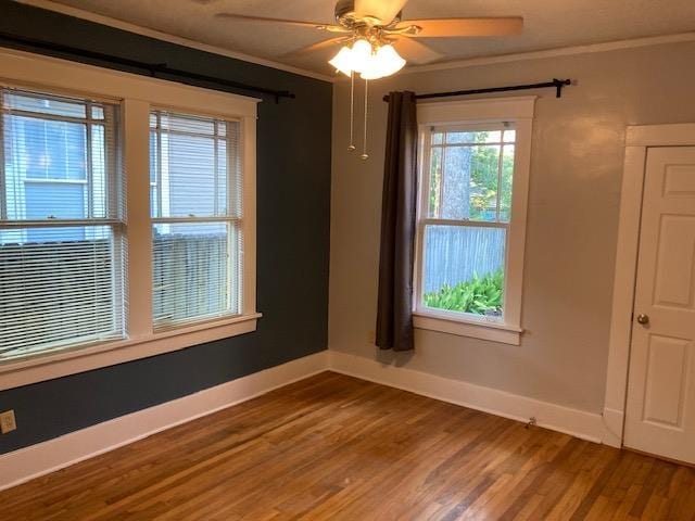 spare room featuring a ceiling fan, crown molding, wood finished floors, and baseboards