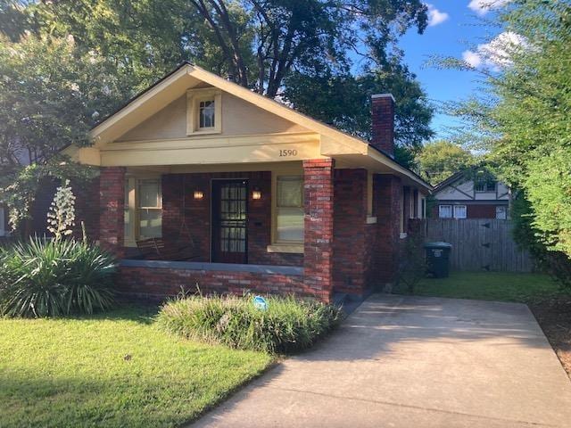 bungalow featuring brick siding, fence, a front yard, covered porch, and a chimney