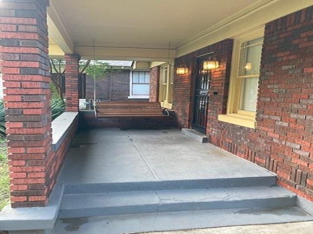 doorway to property featuring an attached carport, a porch, and brick siding