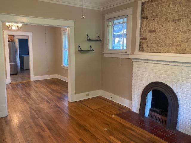 unfurnished living room featuring a brick fireplace, wood finished floors, baseboards, and ornamental molding