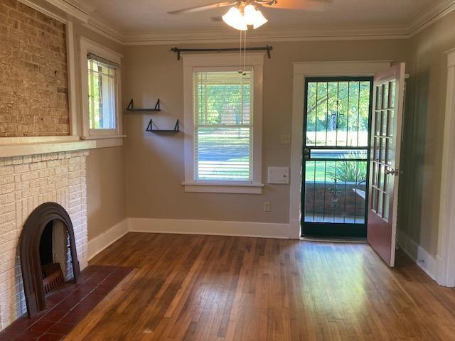 unfurnished living room featuring crown molding, baseboards, ceiling fan, a fireplace, and wood finished floors