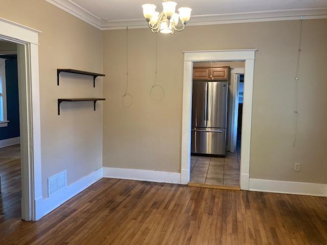 spare room featuring visible vents, crown molding, baseboards, an inviting chandelier, and wood finished floors