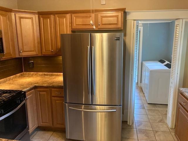 kitchen featuring backsplash, washer and clothes dryer, gas range oven, light tile patterned floors, and freestanding refrigerator