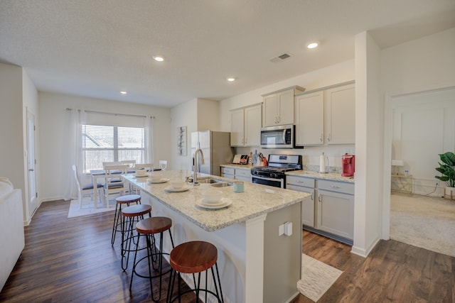 kitchen featuring visible vents, a breakfast bar area, an island with sink, stainless steel appliances, and a sink