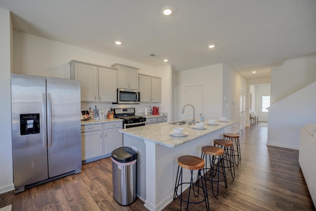 kitchen featuring dark wood-style floors, a center island with sink, a sink, appliances with stainless steel finishes, and a kitchen breakfast bar