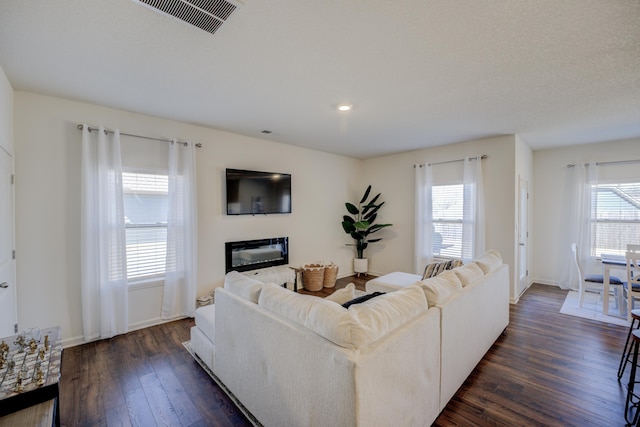 living area featuring visible vents, dark wood-type flooring, baseboards, and a glass covered fireplace