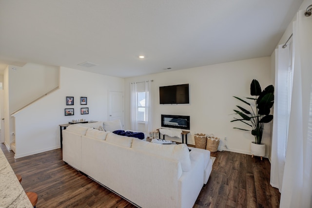 living area featuring stairway, baseboards, a glass covered fireplace, and dark wood-style flooring