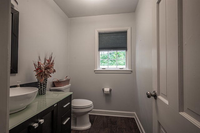 half bath featuring toilet, vanity, baseboards, and wood finished floors