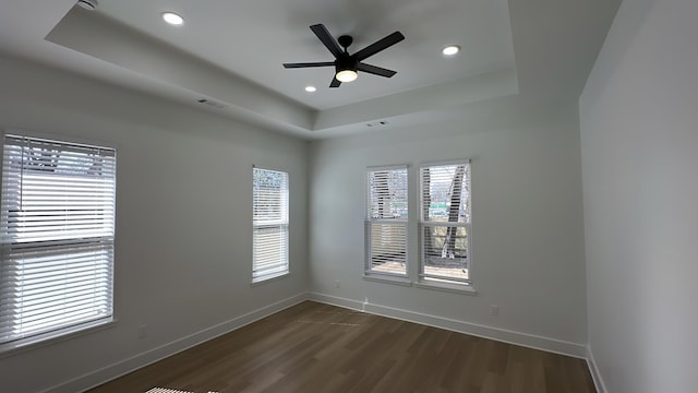 empty room featuring a tray ceiling, baseboards, and dark wood-style flooring