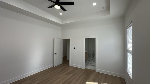 unfurnished bedroom featuring a tray ceiling, ensuite bath, dark wood-type flooring, and baseboards