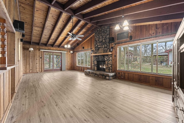 unfurnished living room with wood finished floors, beam ceiling, a stone fireplace, wood ceiling, and wood walls