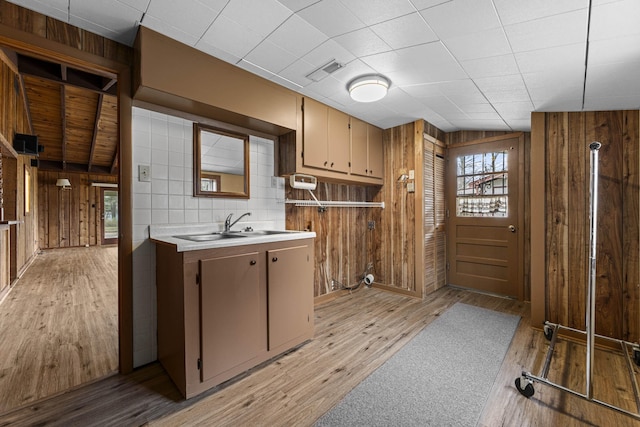 kitchen with light wood finished floors, wooden walls, visible vents, light countertops, and a sink