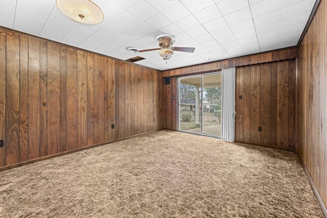 carpeted spare room featuring wood walls, baseboards, and ceiling fan