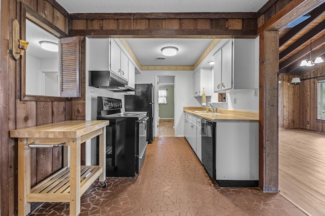 kitchen with wooden walls, a sink, black appliances, under cabinet range hood, and a textured ceiling