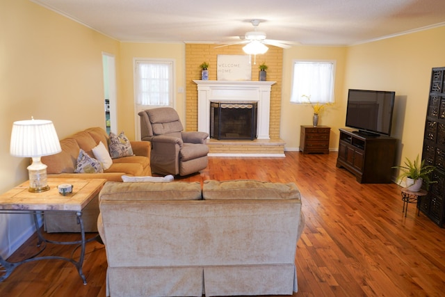 living area featuring ornamental molding, a ceiling fan, wood finished floors, a fireplace, and baseboards