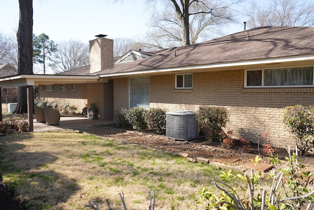 rear view of house with brick siding, cooling unit, a chimney, a yard, and a patio