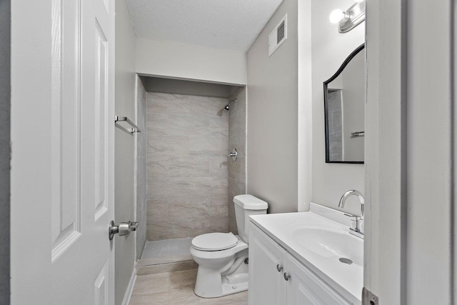 full bath with vanity, visible vents, a tile shower, a textured ceiling, and toilet