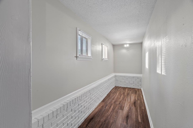 corridor featuring baseboards, a textured ceiling, and dark wood finished floors