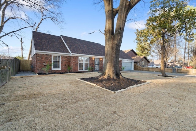 view of front facade with brick siding, fence, concrete driveway, roof with shingles, and a garage