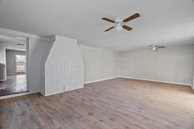 unfurnished room featuring a textured ceiling, wood finished floors, brick wall, and ceiling fan