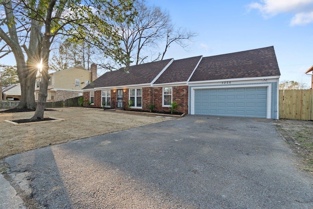 view of front of house with aphalt driveway, fence, a shingled roof, a garage, and brick siding