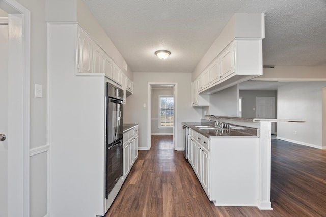 kitchen featuring a peninsula, white cabinets, dark wood-style flooring, and a sink