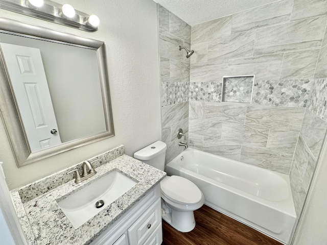 full bath with toilet, wood finished floors, bathing tub / shower combination, a textured wall, and vanity