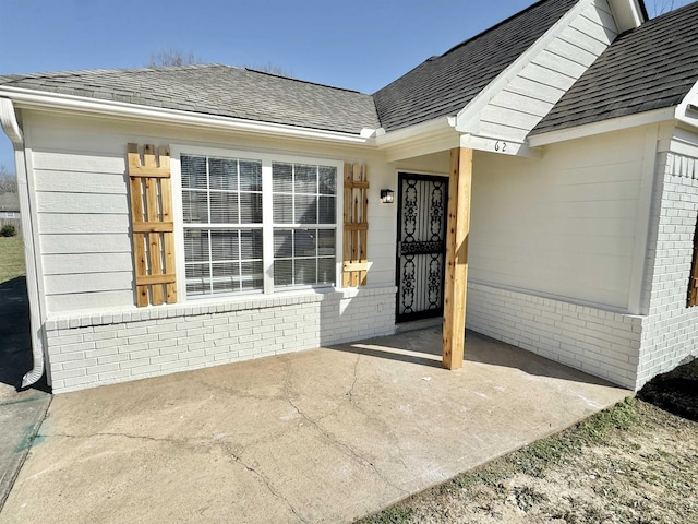 doorway to property with brick siding and a shingled roof