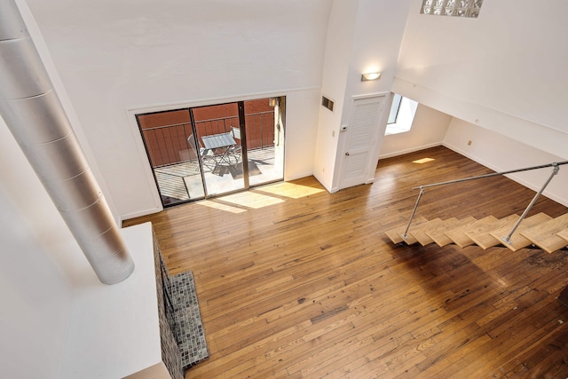 unfurnished living room with hardwood / wood-style floors, baseboards, and high vaulted ceiling