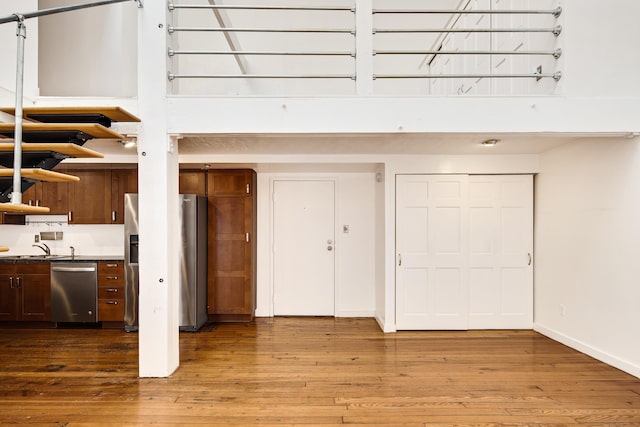 kitchen with a sink, dark countertops, wood finished floors, stainless steel appliances, and baseboards