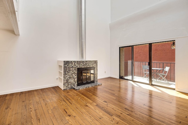 unfurnished living room with baseboards, a towering ceiling, a fireplace, and hardwood / wood-style flooring