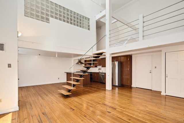 unfurnished living room with visible vents, baseboards, stairway, light wood-style floors, and a towering ceiling