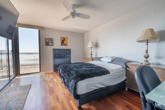 bedroom with a water view, a ceiling fan, a textured ceiling, wood finished floors, and floor to ceiling windows