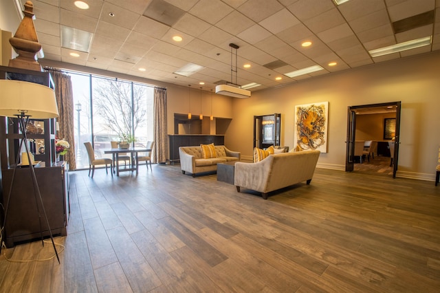 living room featuring a drop ceiling, recessed lighting, baseboards, and wood finished floors