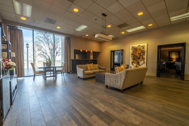 living room featuring dark wood-style floors, a drop ceiling, and baseboards