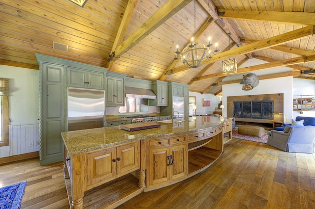 kitchen featuring a glass covered fireplace, hardwood / wood-style floors, stainless steel appliances, wall chimney exhaust hood, and vaulted ceiling with beams