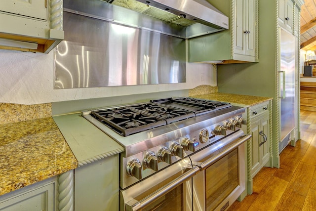 kitchen featuring light stone countertops, extractor fan, high end appliances, and wood finished floors