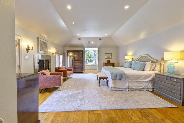 bedroom featuring recessed lighting, lofted ceiling, wood finished floors, and a tiled fireplace